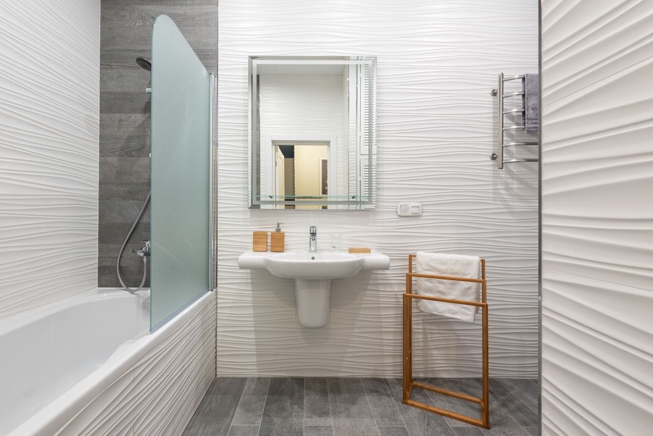 A bright modern bathroom with white tile, polished fixtures and folded towels