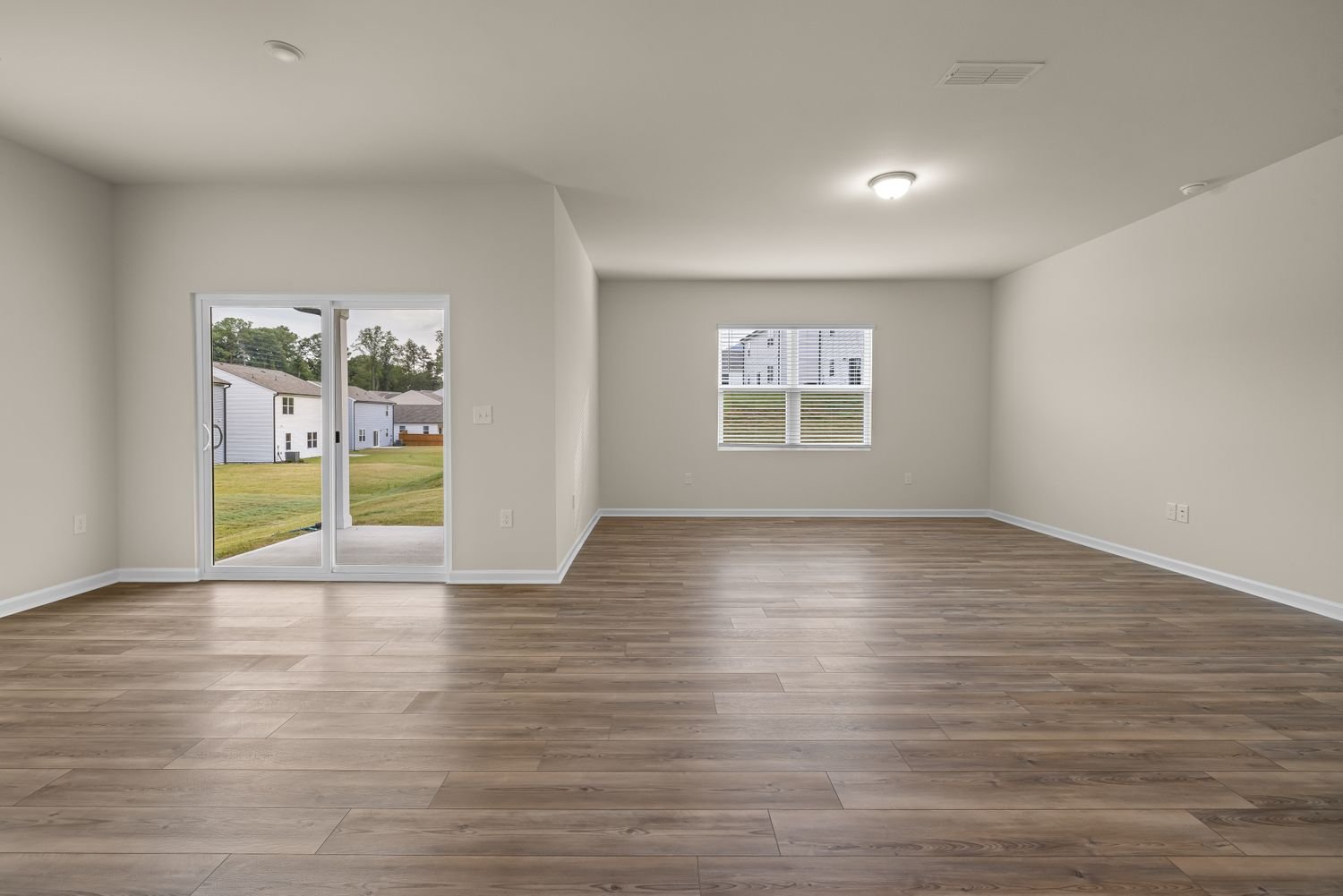 An empty, freshly cleaned room with wood floors and a view to a green suburban yard